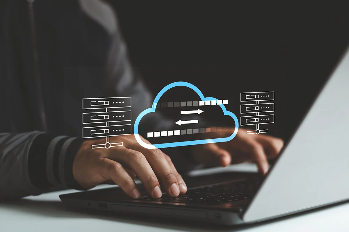 A person typing on a laptop at a desk, with an overlay illustration of a cloud, showing the concept of data backup and recovery services